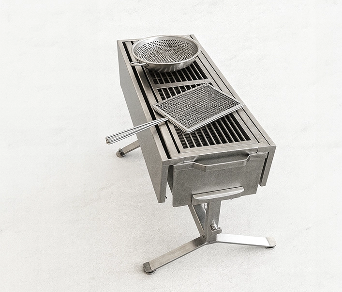 Barbacoa estrecha de acero inoxidable sobre pie central con cesta y bol perforado colocados sobre la parrilla.