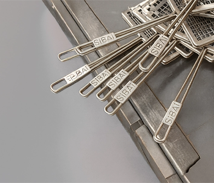 Detalle de varios pinchos de acero inoxidable con el logotipo SiBAi grabado en el mango, apoyados en la esquina de una parrilla metálica.